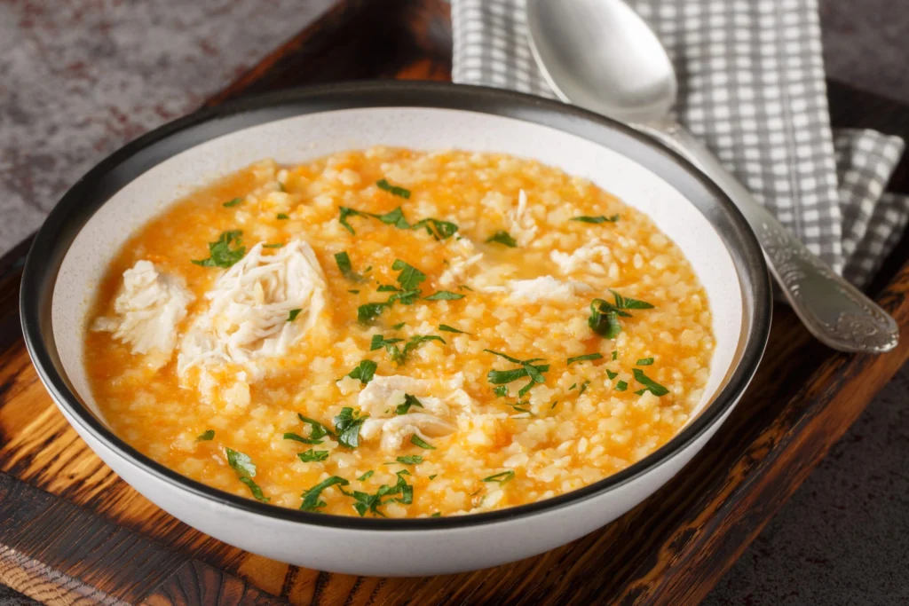 Hearty pastina soup with shredded chicken and parsley in a ceramic bowl