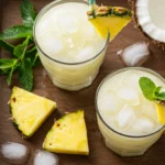 Two glasses of Virgin Piña Colada with pineapple wedges, mint, and striped straws on a wooden tray