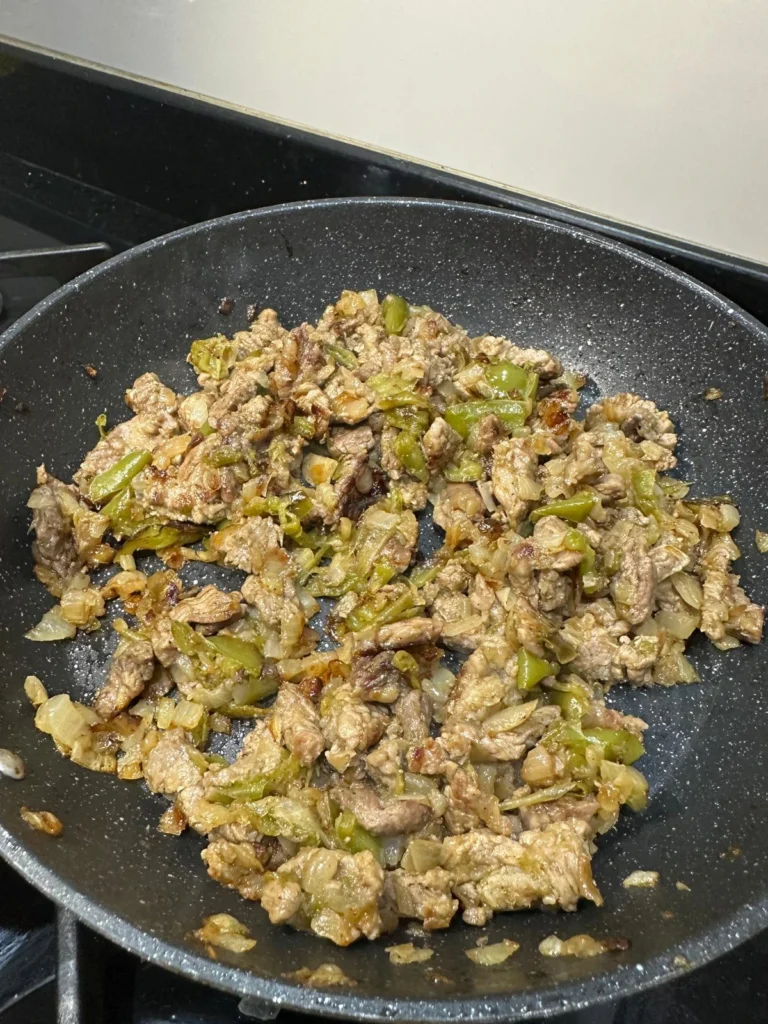browned ribeye pieces with sautéed onions and green bell peppers in a nonstick skillet for philly cheesesteak
