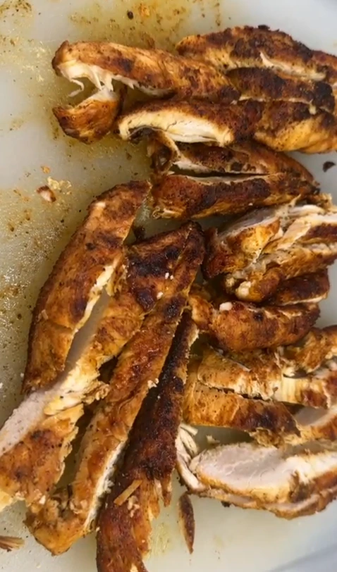 Sliced, pan-seared chicken with a smoky spice crust on a cutting board, ready for burrito filling.