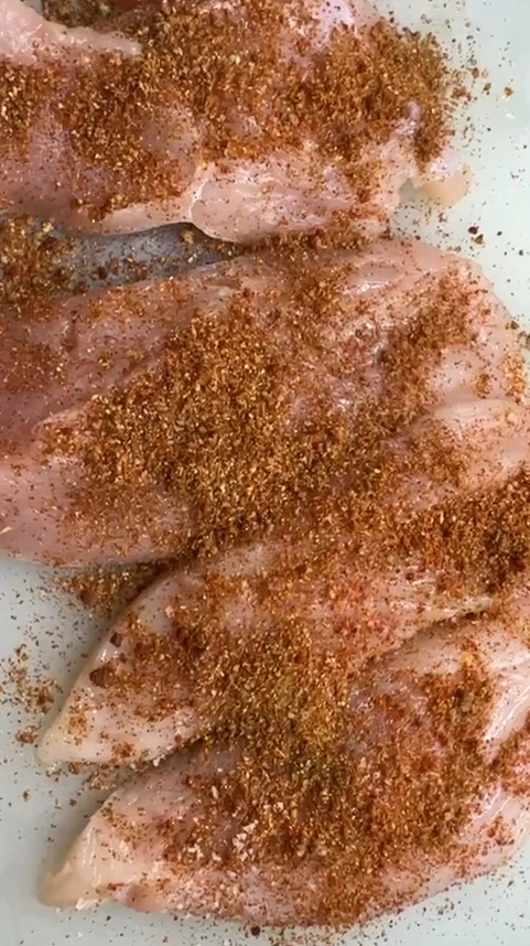 Raw chicken breasts coated with taco-style seasoning, ready to cook for chicken burrito filling.