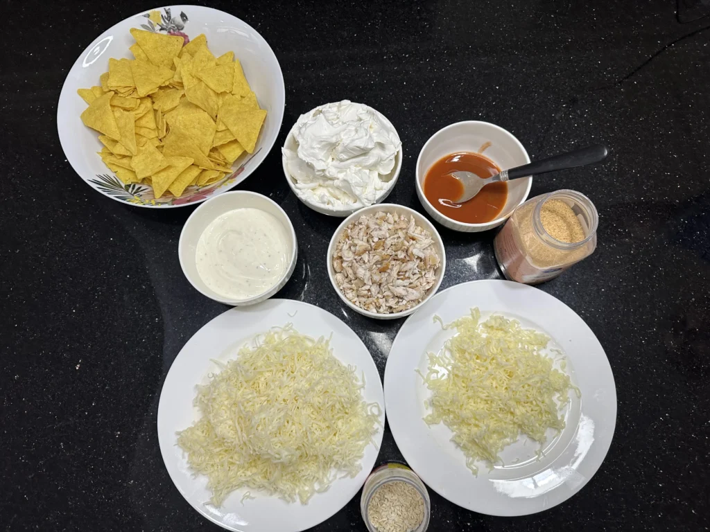 Ingredients for Buffalo chicken dip including shredded chicken, cream cheese, Buffalo sauce, ranch, shredded cheese, tortilla chips, garlic powder, and onion flakes