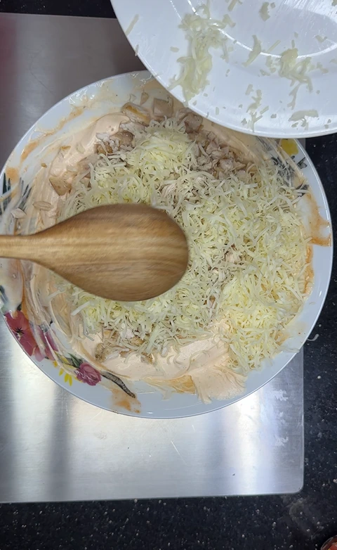 Shredded cheese added over cooked chicken in the Buffalo chicken dip mixture