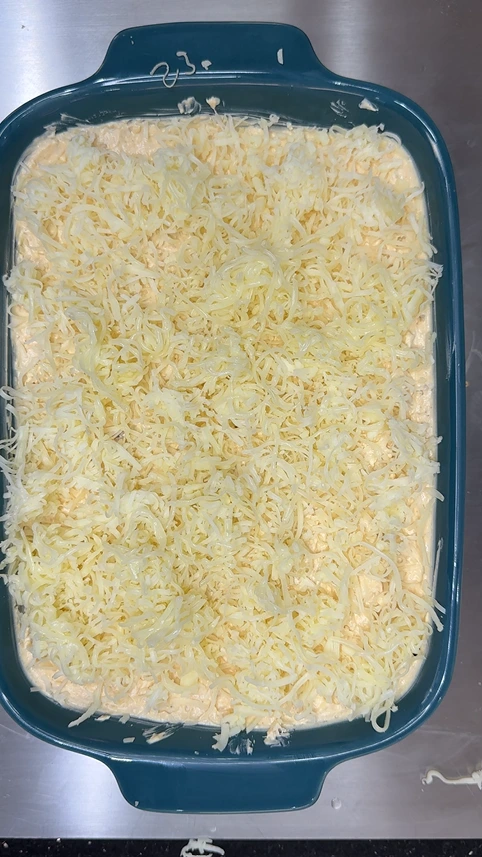 Buffalo chicken dip spread in a baking dish and topped with shredded cheese before baking