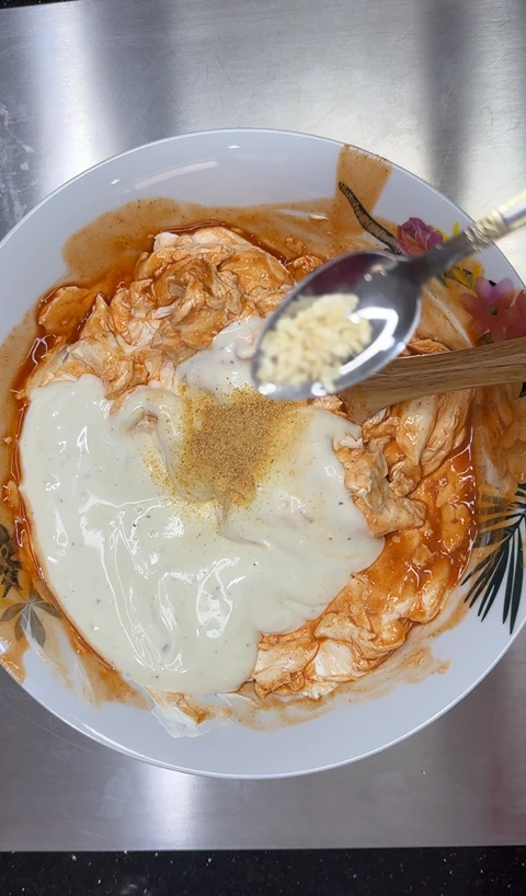 Garlic powder being added to the Buffalo chicken dip cream cheese base with ranch, Buffalo sauce, and onion powder